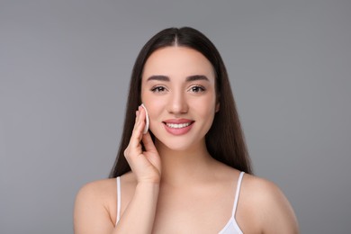 Beautiful woman removing makeup with cotton pad on gray background