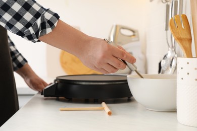 Photo of Man cooking delicious crepe on electric pancake maker in kitchen, closeup
