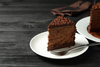 Piece of delicious chocolate truffle cake and fork on black wooden table, space for text