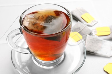 Photo of Tea bags and cup of aromatic drink on white table, closeup