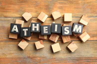 Image of Word Atheism made of black cubes with letters on wooden table, flat lay
