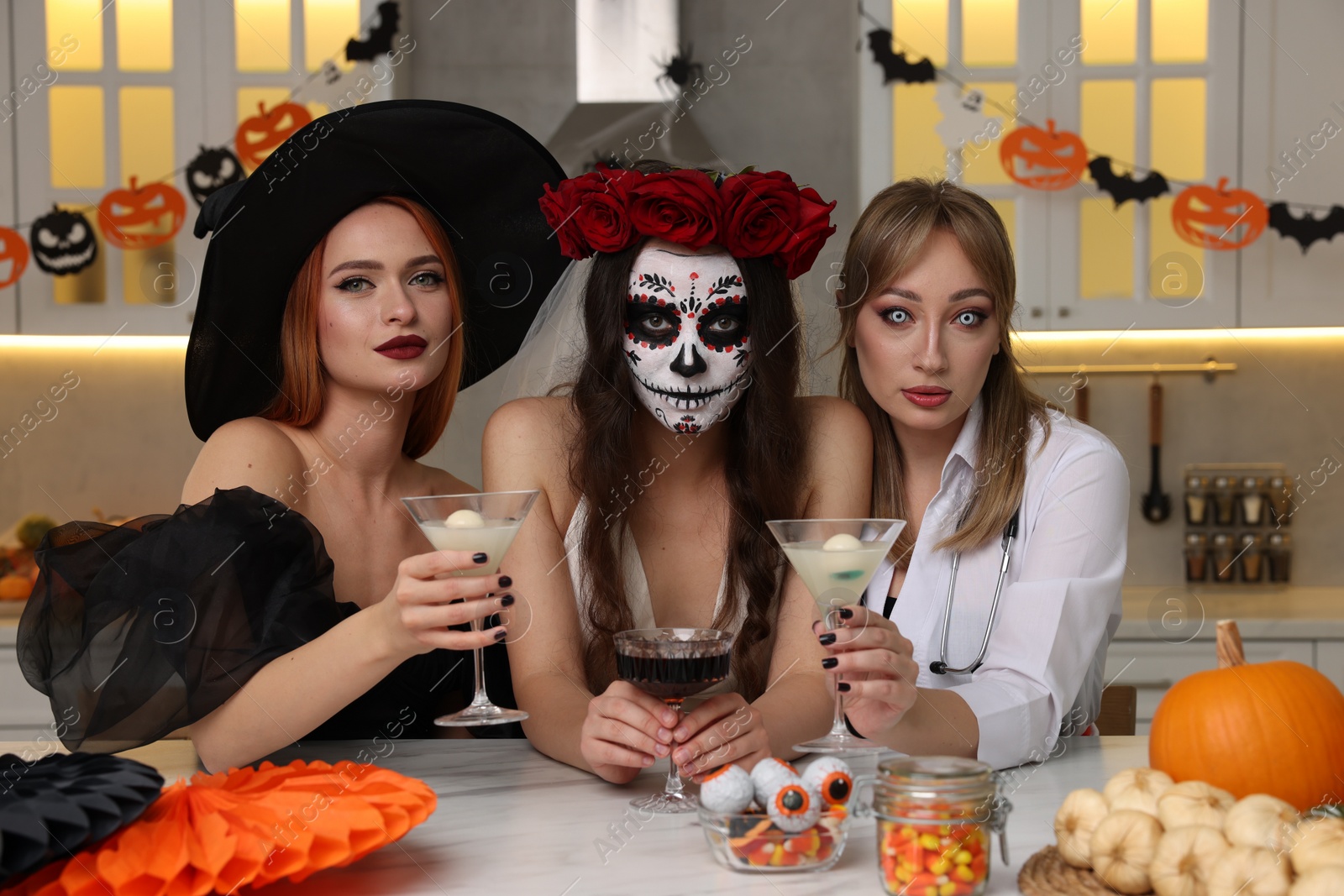 Photo of Group of women in scary costumes with cocktails celebrating Halloween indoors