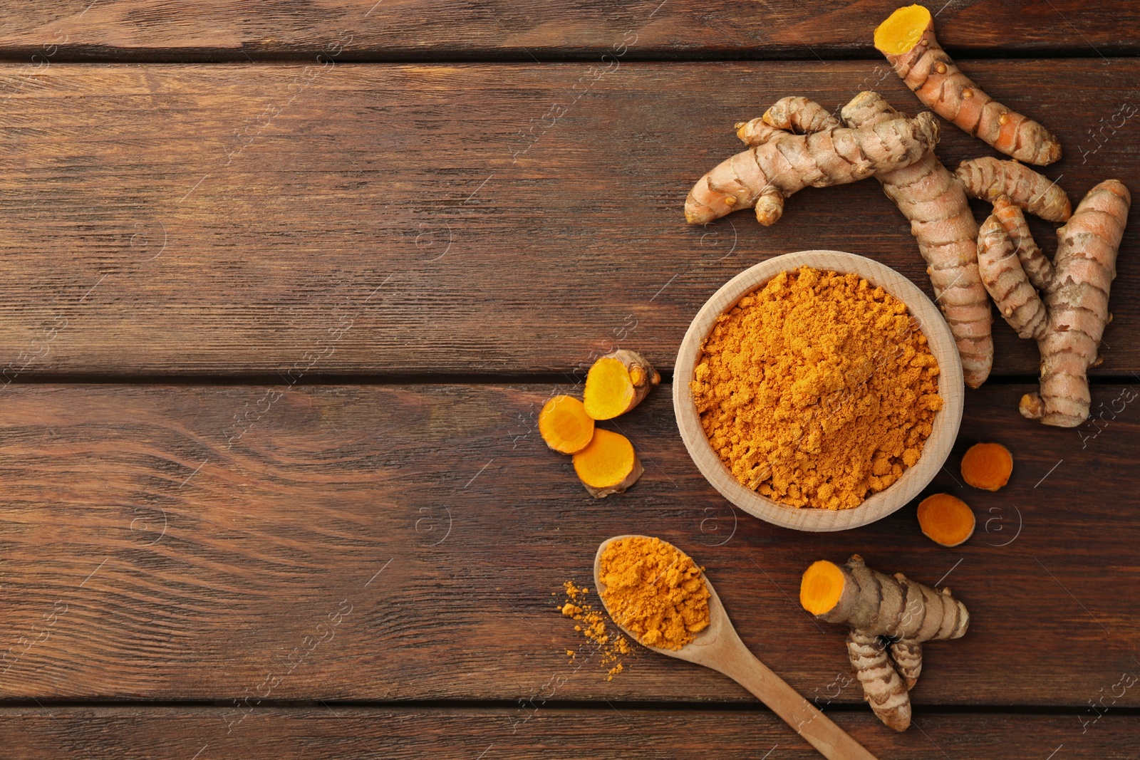 Photo of Aromatic turmeric powder and raw roots on wooden table, flat lay. Space for text