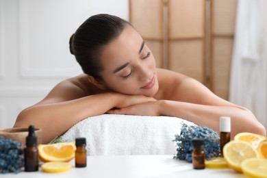 Beautiful young woman relaxing on massage couch and bottles of essential oil with ingredients on table in spa salon