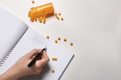 Photo of Woman writing word PSYCHO in notebook near jar of pills on table, closeup. Space for text