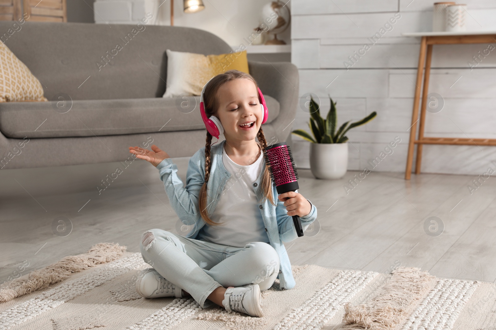 Photo of Cute little girl in headphones with hairbrush singing at home