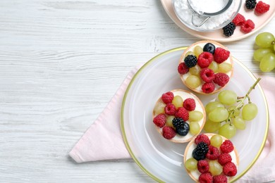 Delicious tartlets with berries on white wooden table, flat lay. Space for text