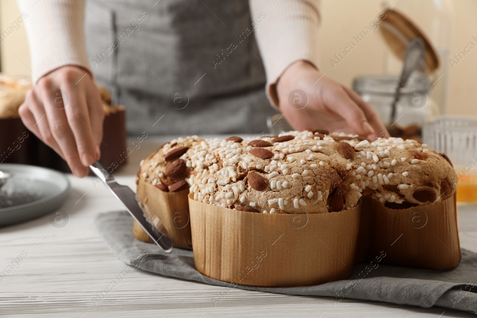 Photo of Woman cutting delicious Italian Easter dove cake (traditional Colomba di Pasqua) at white wooden table, closeup