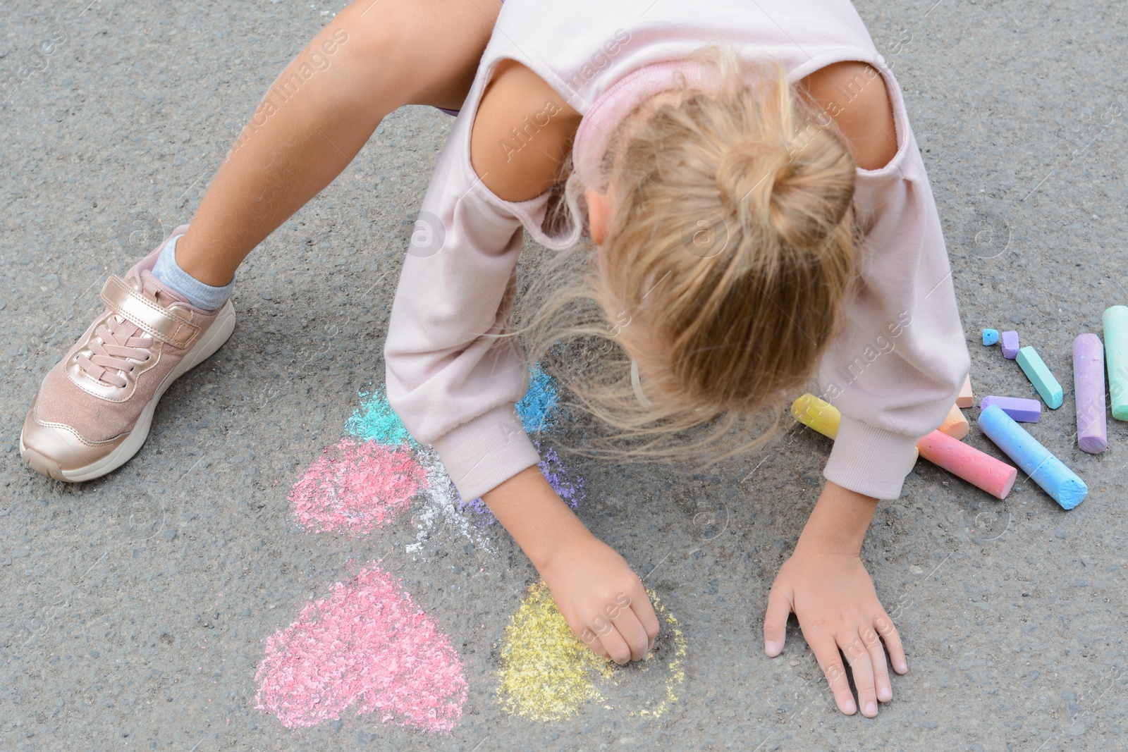 Photo of Little child drawing butterfly and hearts with chalk on asphalt