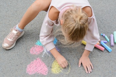 Little child drawing butterfly and hearts with chalk on asphalt