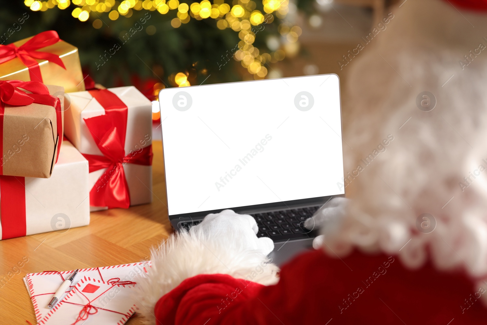 Photo of Santa Claus using laptop, closeup. Christmas gifts and letters on table indoors