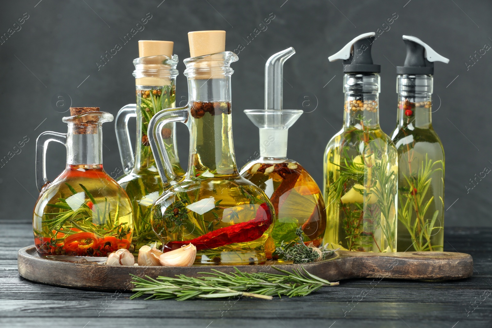 Photo of Cooking oil with different spices and herbs in bottles on grey wooden table