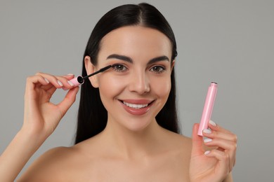 Photo of Beautiful young woman applying mascara on grey background