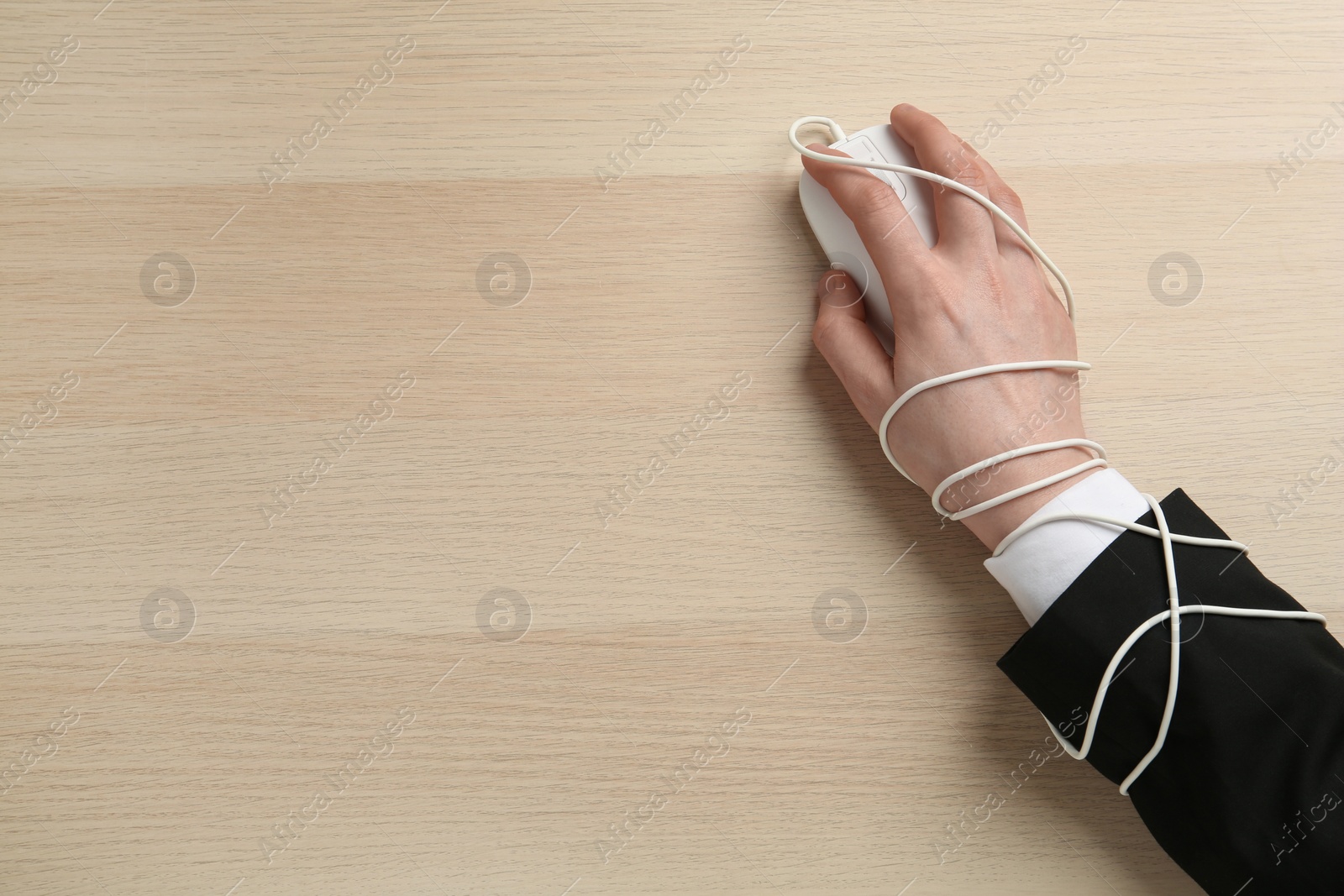 Photo of Internet addiction. Top view of man using computer mouse cable at wooden table, hand tied to device