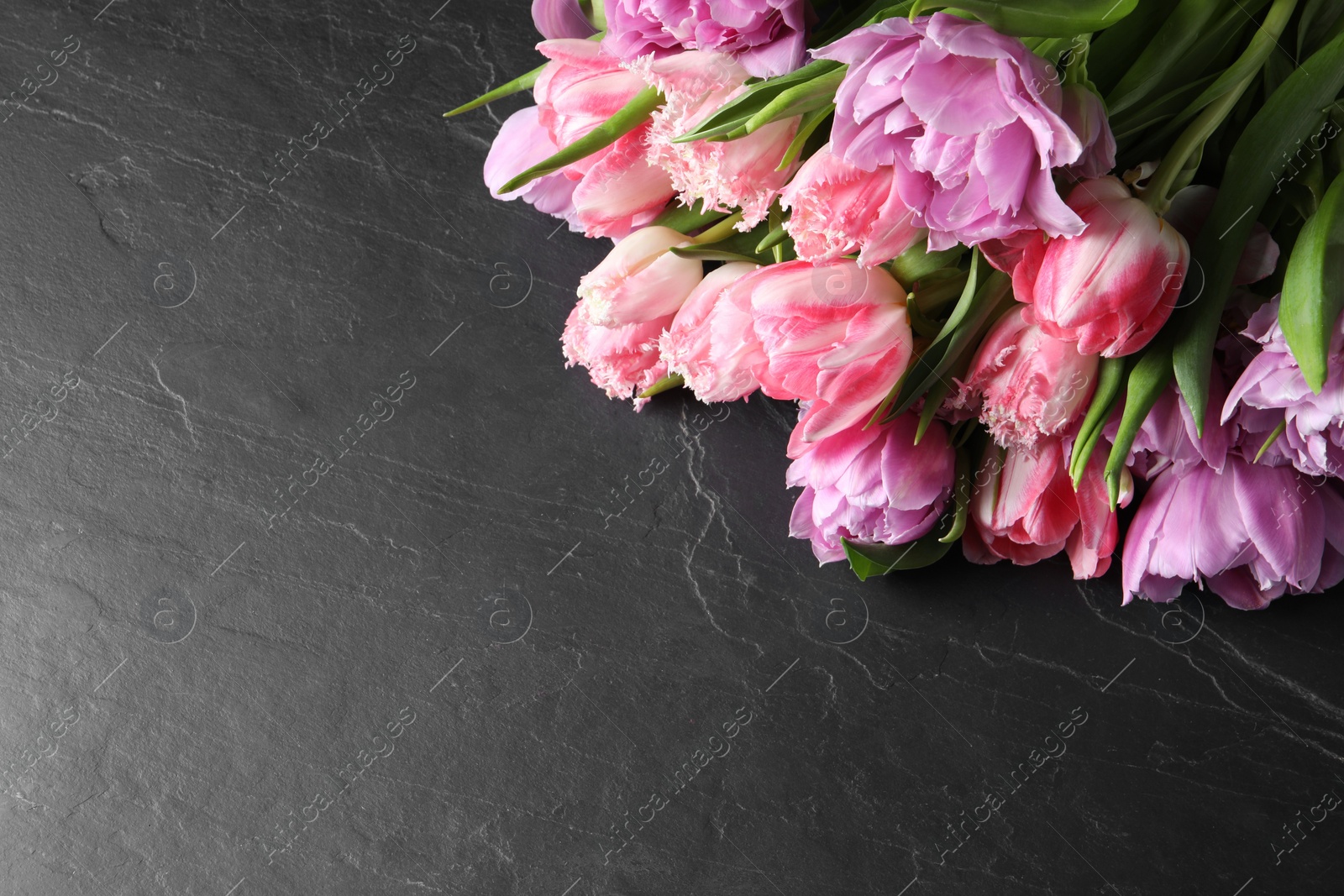 Photo of Beautiful bouquet of colorful tulip flowers on black table top view. Space for text
