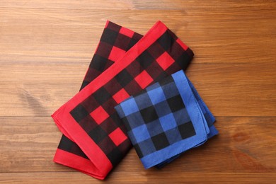 Folded red and blue checkered bandanas on wooden table, flat lay