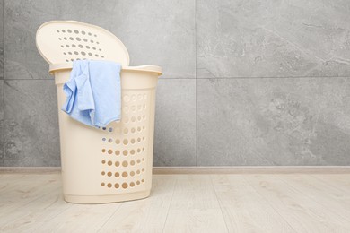 Photo of Plastic laundry basket with clothes near grey wall. Space for text