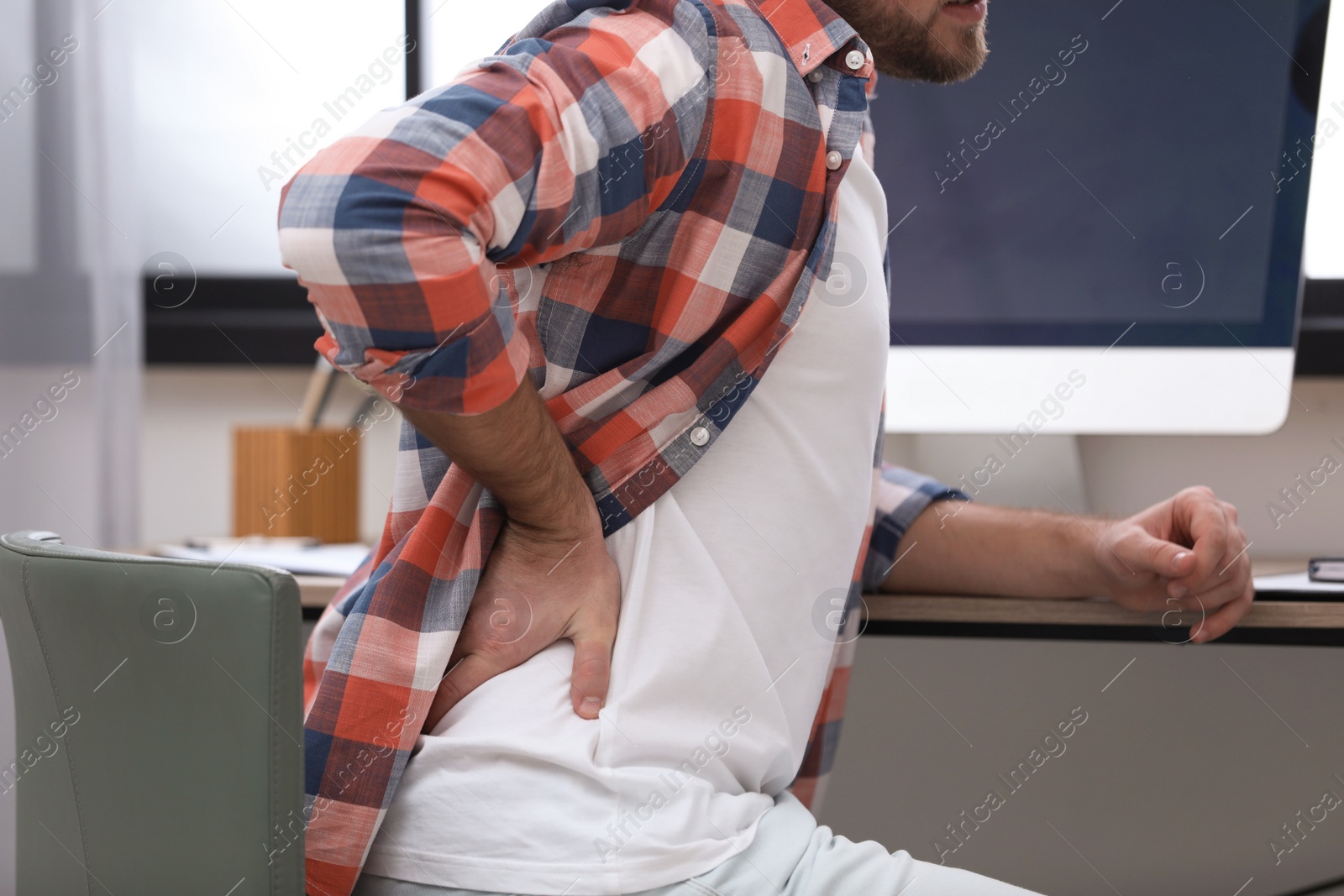 Photo of Young man suffering from back pain in office, closeup