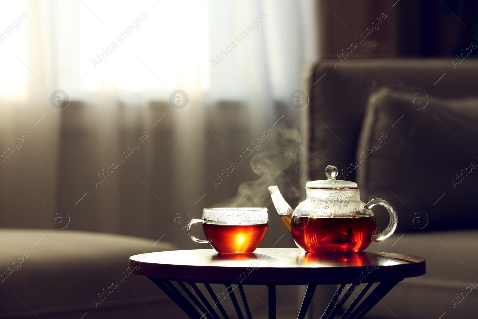 Photo of Teapot and cup of fresh hot tea on table against blurred background. Space for text