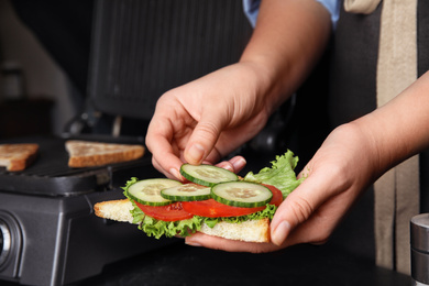 Photo of Woman adding cucumber to sandwich at black table, closeup