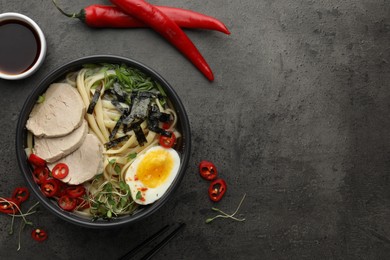 Photo of Delicious ramen with meat in bowl and ingredients on grey textured table, flat lay. Space for text. Noodle soup