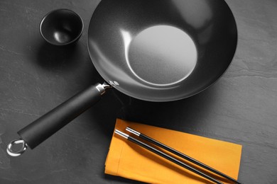 Empty iron wok, sauce bowl and chopsticks on black table