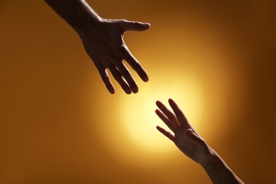 Photo of Man reaching for woman's hand on color background, closeup. Help and support concept