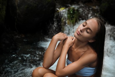 Photo of Beautiful young woman in light blue bikini relaxing on rock near mountain stream outdoors. Space for text