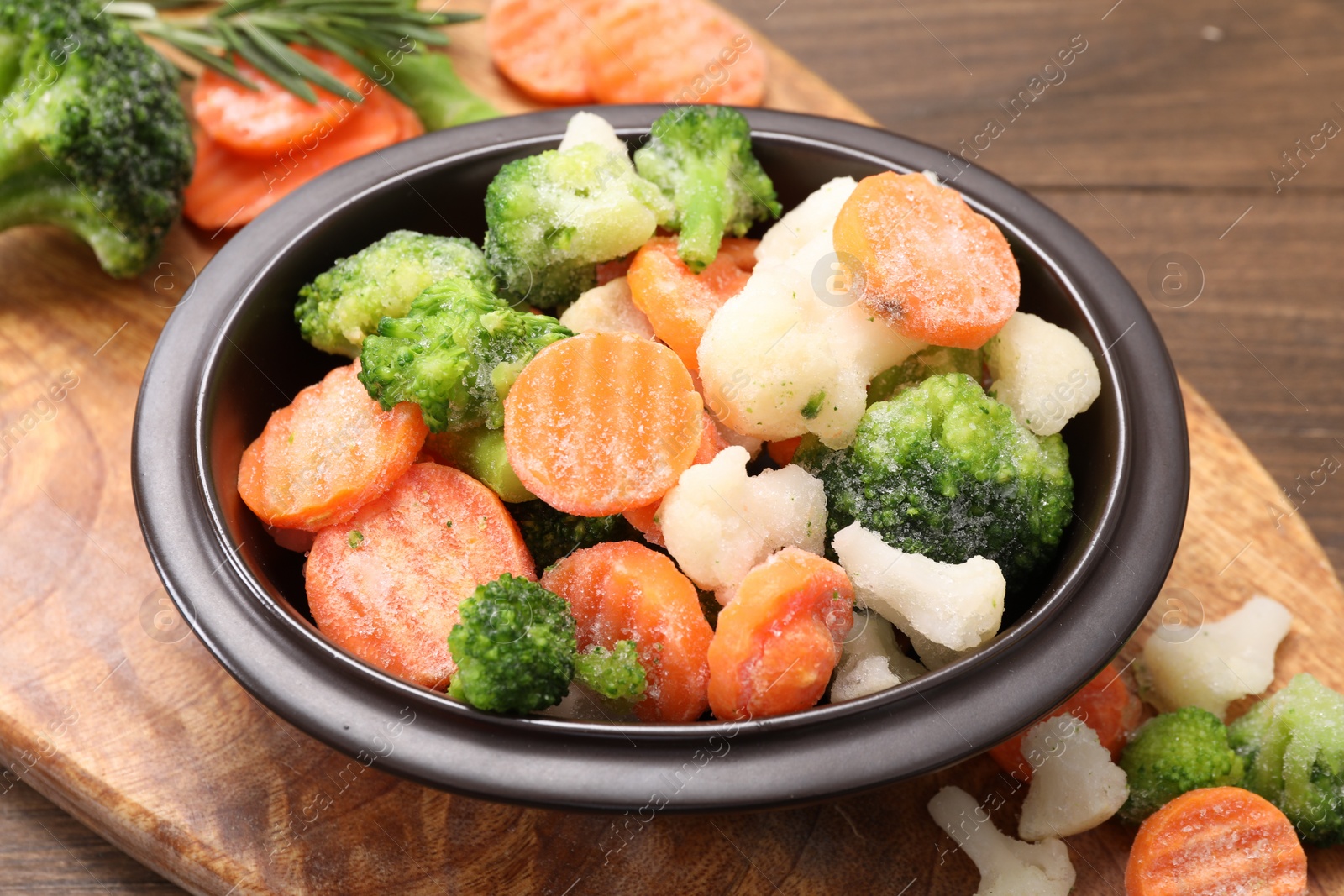 Photo of Mix of different frozen vegetables in bowl on wooden table, closeup