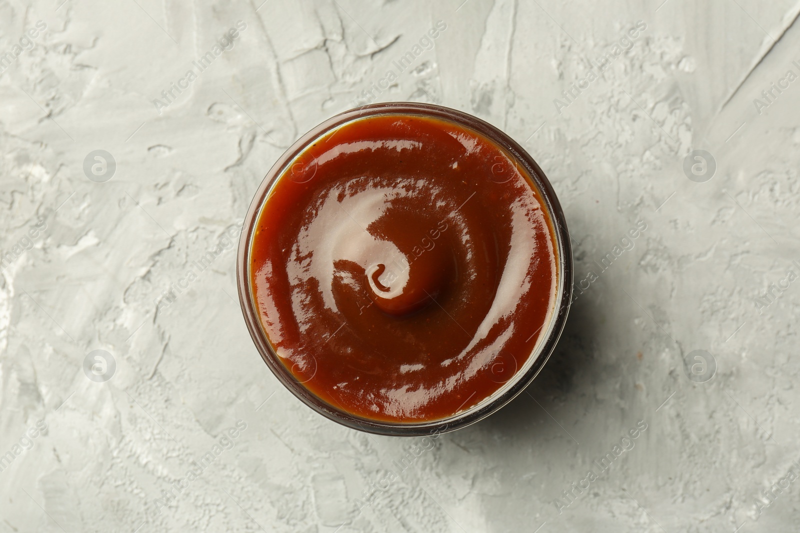 Photo of Tasty barbeque sauce in bowl on grey textured table, top view