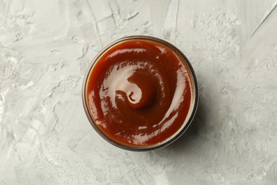 Tasty barbeque sauce in bowl on grey textured table, top view