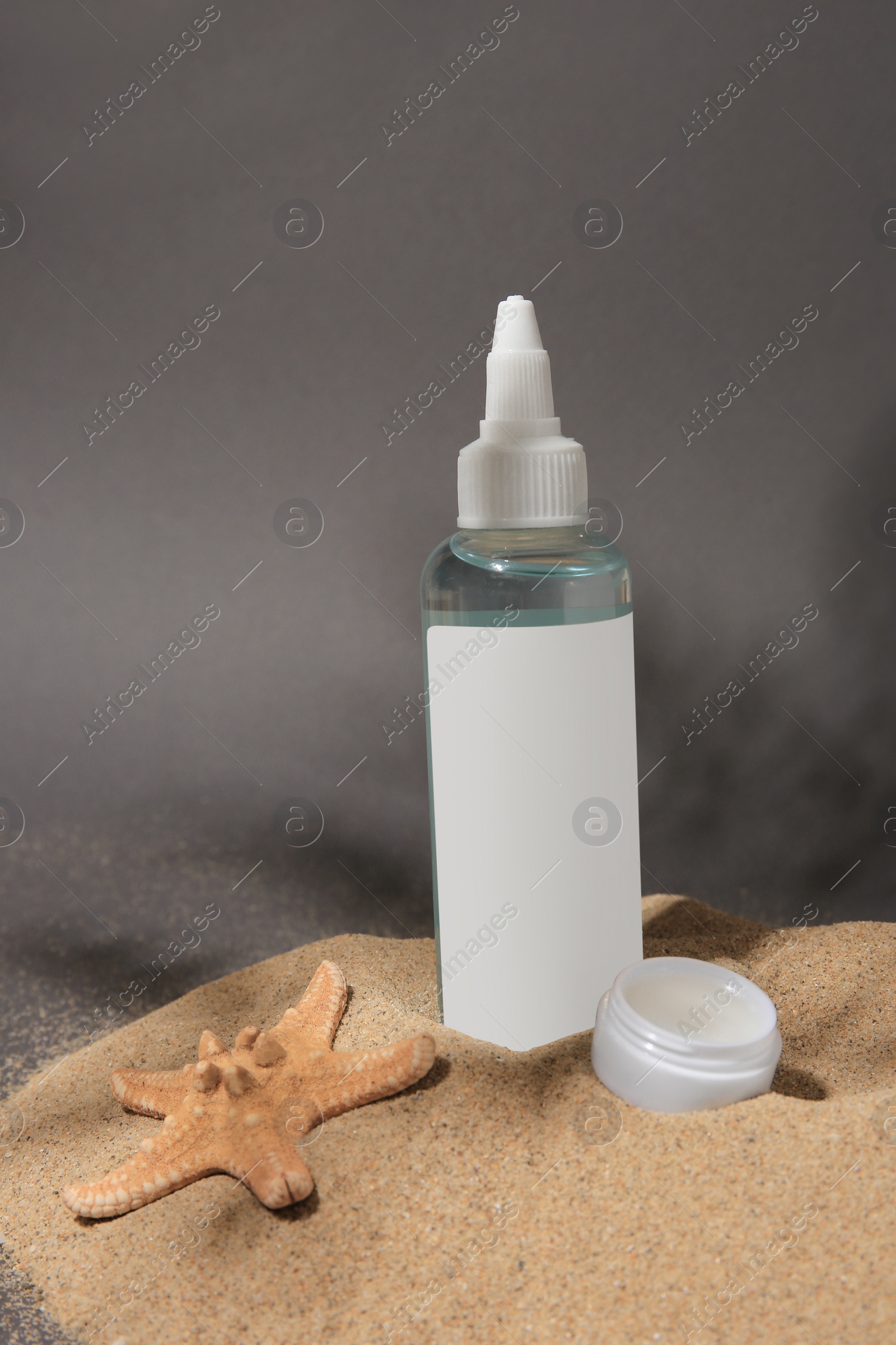 Photo of Cosmetic products and starfish on sand against grey background