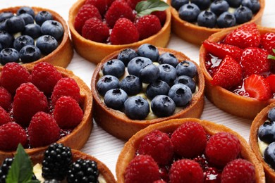 Tartlets with different fresh berries on white wooden table, closeup. Delicious dessert