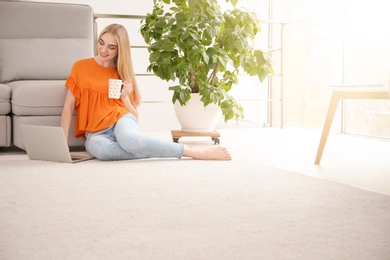 Photo of Young woman with laptop sitting on floor at home