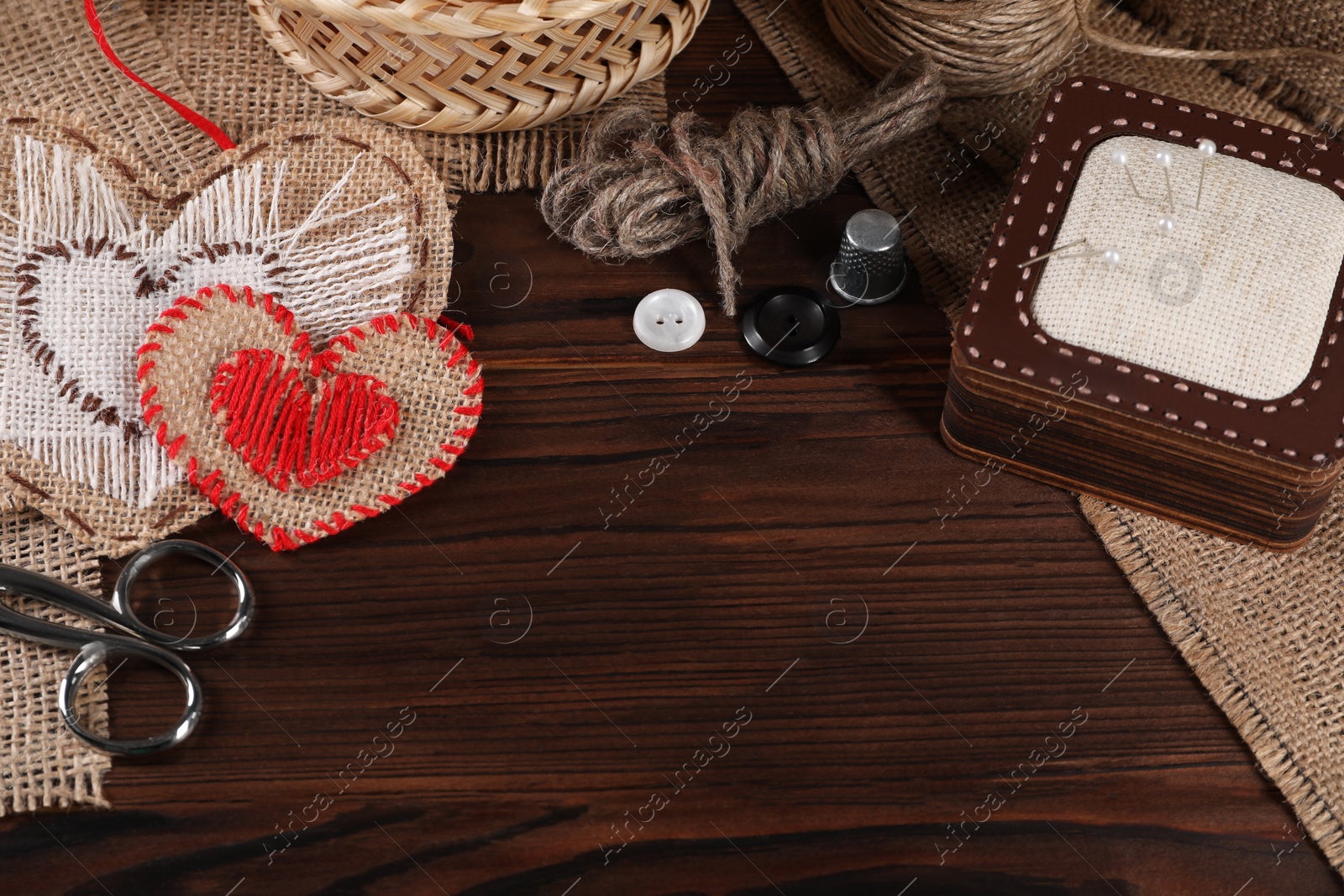 Photo of Heart shaped pieces of burlap fabric with different stitches and sewing tools on wooden table, above view. Space for text