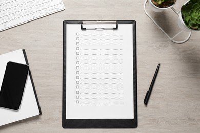 Photo of Clipboard with checkboxes, smartphone, plants and computer keyboard on white wooden table, flat lay. Checklist