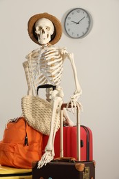 Photo of Waiting concept. Human skeleton in hat with suitcases indoors