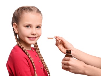 Mother giving syrup to her daughter from dosing spoon against white background