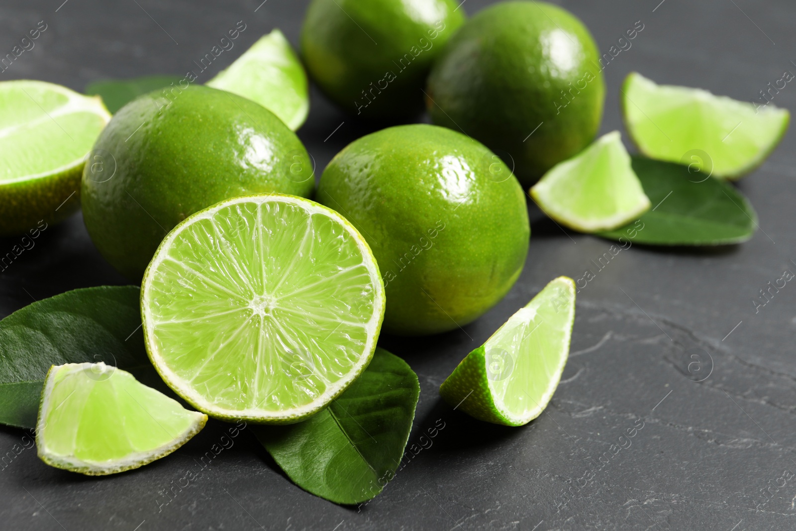 Photo of Fresh ripe limes and leaves on black table, closeup