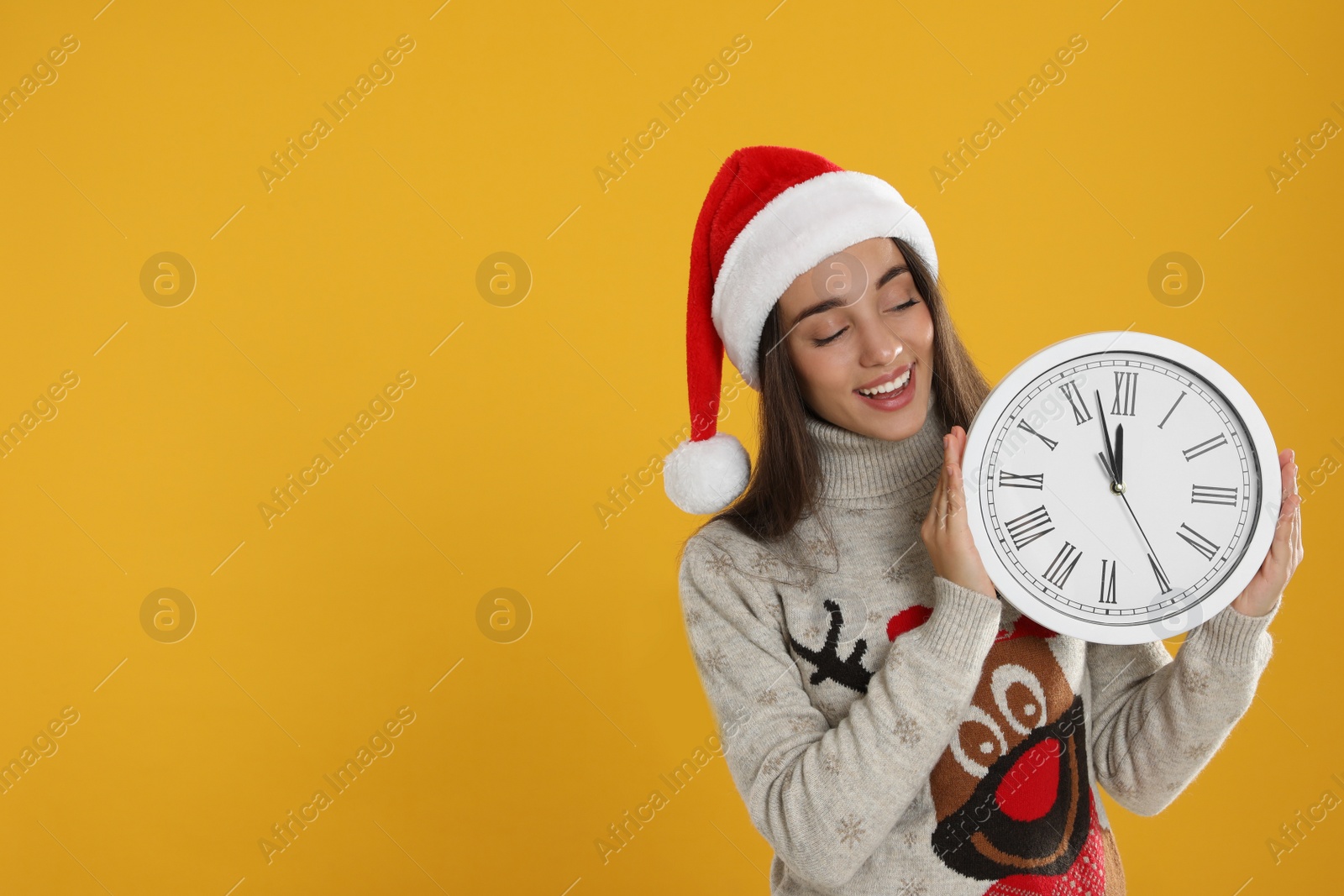 Photo of Woman in Santa hat with clock on yellow background, space for text. New Year countdown