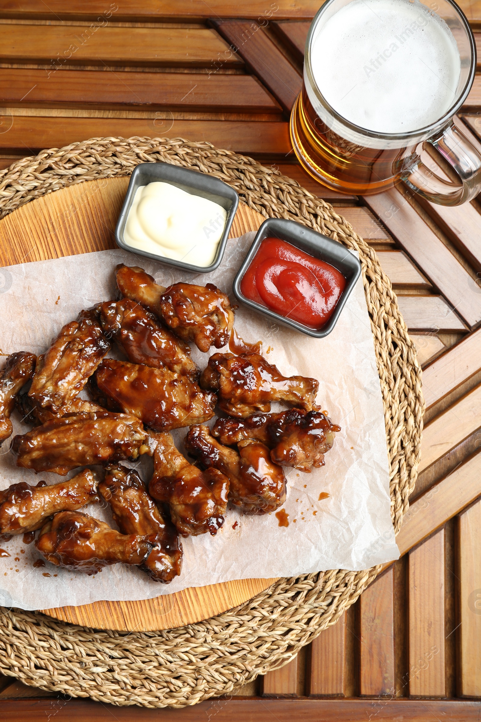 Photo of Tasty chicken wings, mug of beer and sauces on wooden table, flat lay. Delicious snack