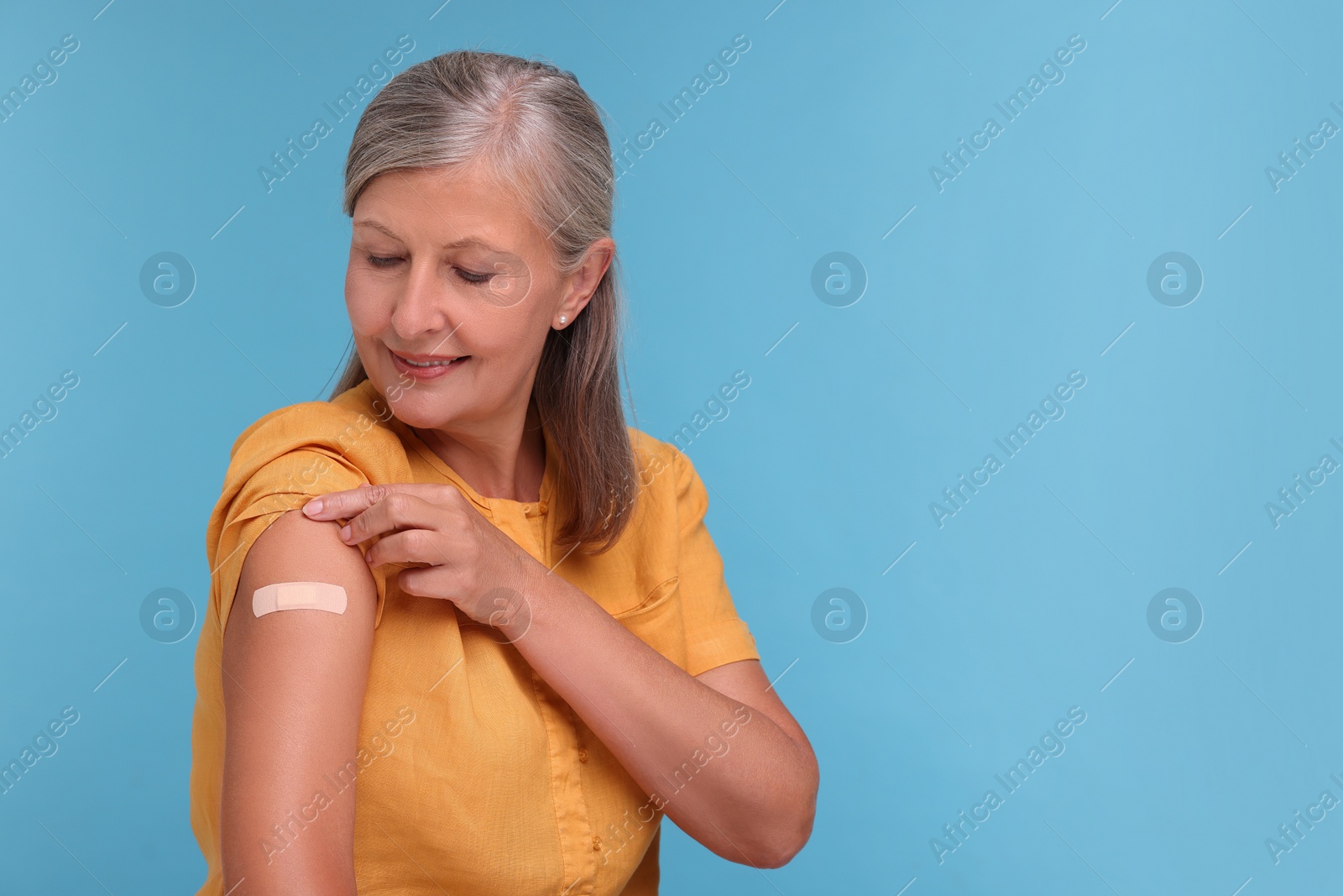 Photo of Senior woman with adhesive bandage on her arm after vaccination against light blue background, space for text