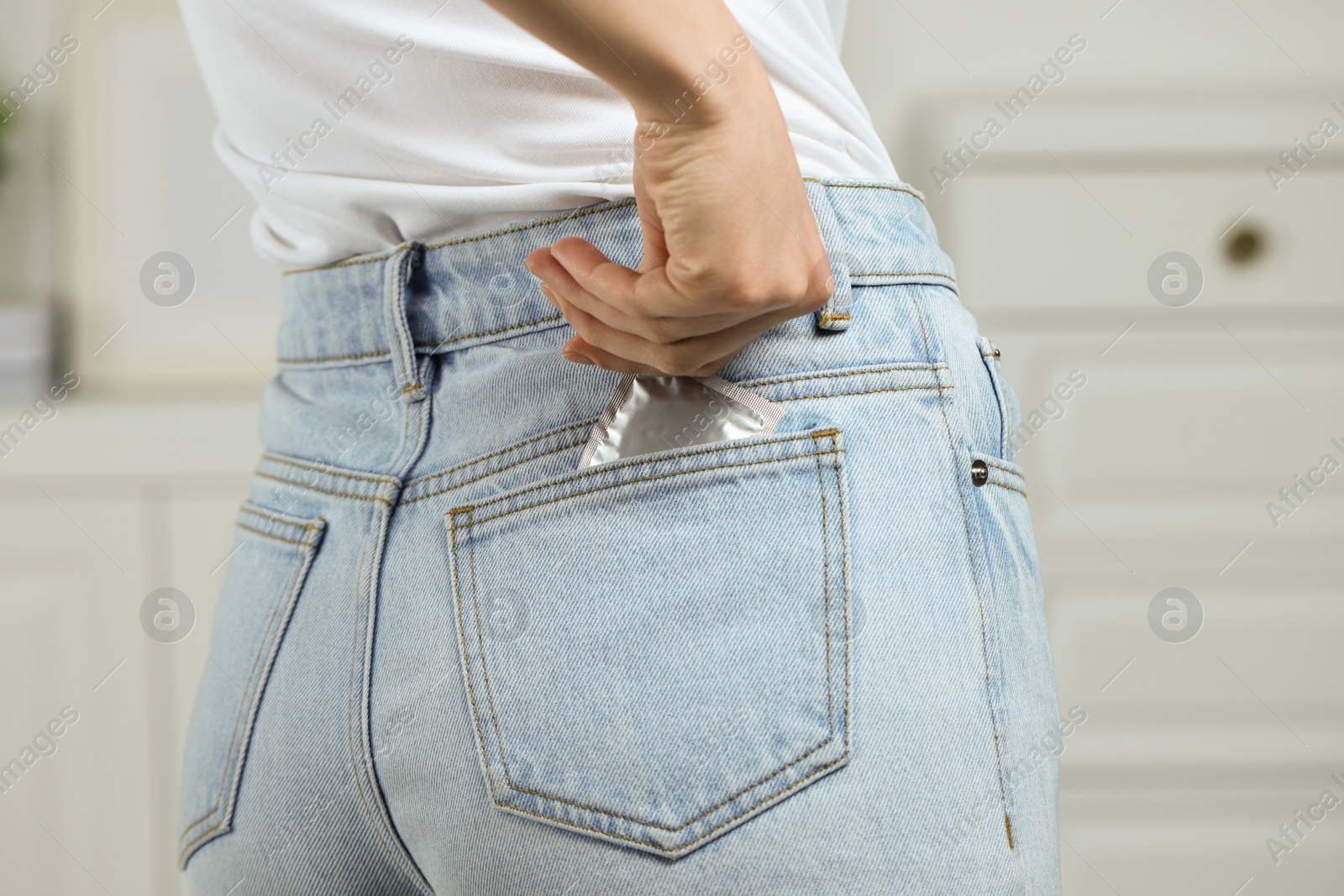 Photo of Woman pulling condom out of pocket indoors, closeup. Safe sex