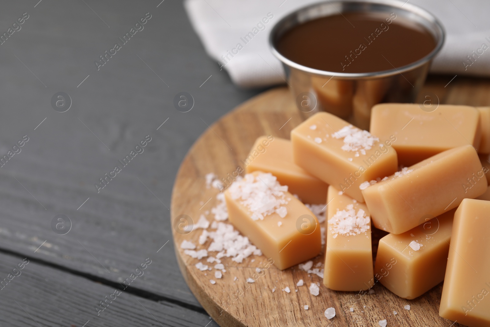 Photo of Yummy caramel candies and sea salt on wooden table, closeup. Space for text