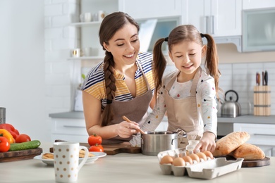 Photo of Young nanny with cute little girl cooking together in kitchen