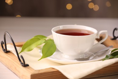 Photo of Aromatic tea in cup, saucer, spoon and green leaves on table