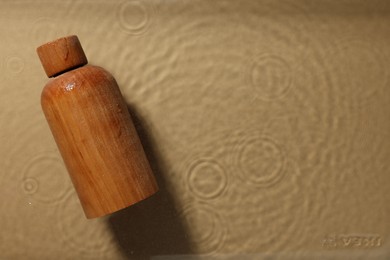 Photo of Wooden bottlecosmetic product in water on beige background, top view. Space for text