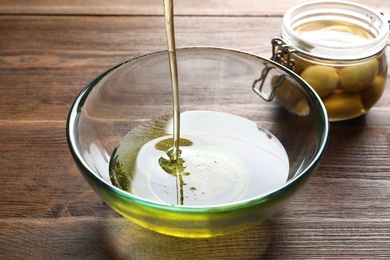 Photo of Pouring fresh olive oil into bowl on wooden background