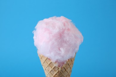 Photo of Sweet cotton candy in waffle cone on light blue background, closeup