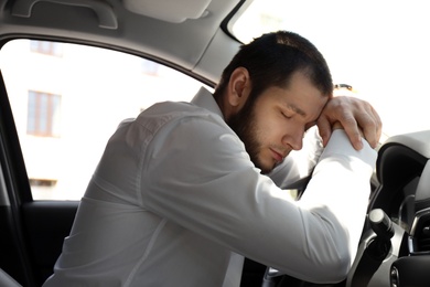 Photo of Tired man sleeping on steering wheel in his modern car